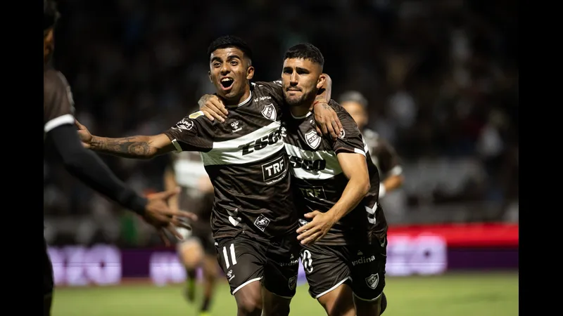 Cầu thủ của Platense đi bóng qua cầu thủ của Deportivo Riestra trong trận đấu bóng đá